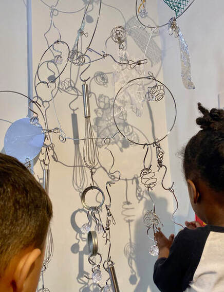 Children working on a hanging sculpture of metal household items